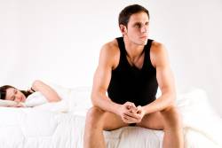 man sitting on bed with partner asleep after failing to reach orgasm because of delayed ejaculation